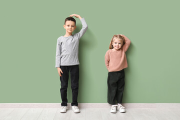 Cute little children measuring height near green wall