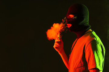 Handsome young man in balaclava with disposable electronic cigarette on black background