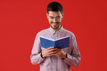 Young man reading book on red background