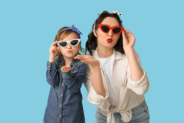 Beautiful pin-up woman and her daughter in sunglasses blowing kiss on blue background - obrazy, fototapety, plakaty