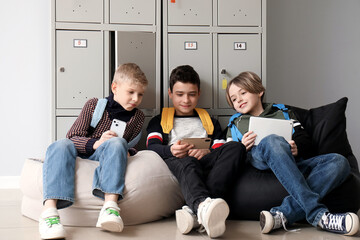 Little schoolboys using gadgets near locker at school