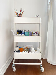 Paint brushes, spatula, paint tubes, and artist material in a studio. Art supplies. Creative tools in a mobile cart.