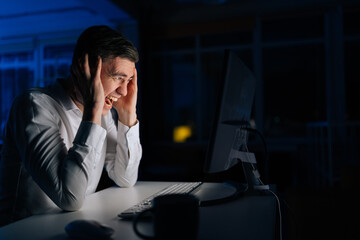 Angry office worker male working late at night and looking at computer while screaming alone....