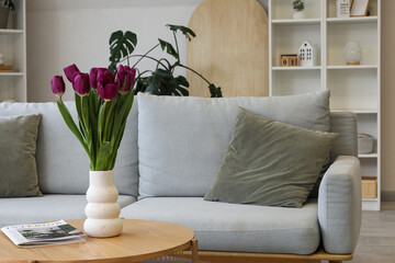 Modern interior of light living room with cozy sofa and tulips