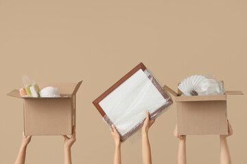 Women with moving boxes and wrapped things on beige background
