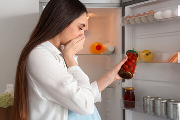 Young pregnant woman feeling bad smell from canned tomatoes near fridge in kitchen