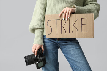 Protesting female photographer holding placard with text STRIKE and photo camera on grey background