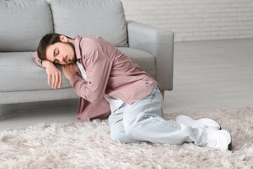 Tired young man sleeping beside sofa at home - obrazy, fototapety, plakaty
