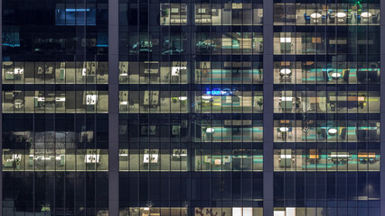 Office building exterior during late evening with interior lights on and people working inside night timelapse