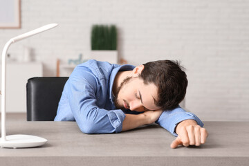 Tired young businessman sleeping at table in office - obrazy, fototapety, plakaty