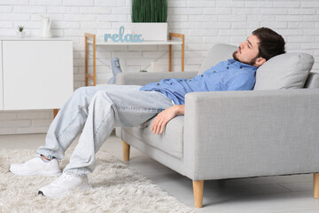Tired young man sleeping on couch at home - obrazy, fototapety, plakaty