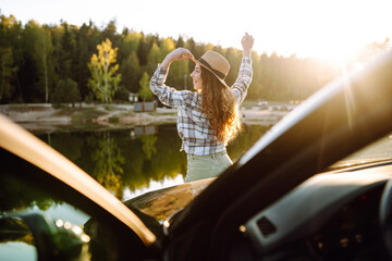 Young woman standing near the car in sunny day, travel by car  in the nature, freedom. Active lifestyle.