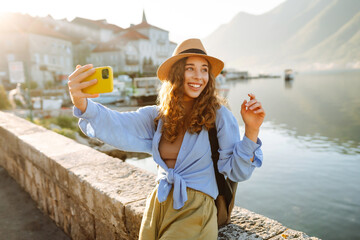 Beautiful tourist walks the streets and takes selfie using smartphone camera. Lifestyle, travel,...