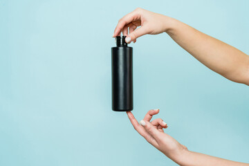 Woman's hand holding black bottle of cosmetic product for shower on blue background