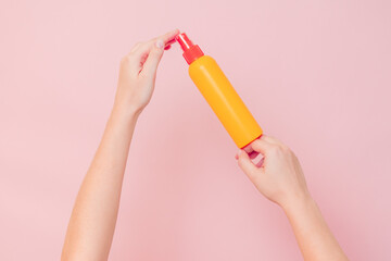 Hand holding plastic spray bottle (as mineral spray or hair spray) on pink background. Cosmetics beauty mockup for product branding