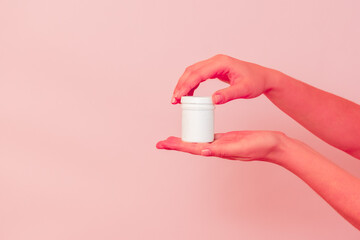Hand with blank white plastic tube on pink background. Cosmetics beauty mockup for product branding