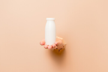 Hand holding bottle of probiotic yogurt for digestive system with beige background. Dietary supplements for stomach