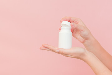 White bottle plastic tube in woman's hands on pink background. Packaging for pills, capsules or supplements. Cosmetics