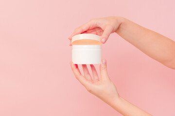 Hand holding jar of cosmetic cream on pink background. Cosmetics beauty mockup for product branding