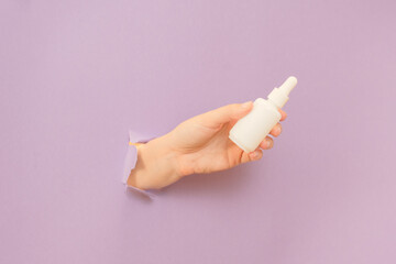 Hand holding glass bottle with dropper lid. White container with cosmetic product, serum (essential oil ) on lilac background. Concept of beauty