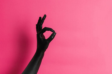 Black painted elegant woman's hand on her skin gesticulates on pink background. High Fashion art concept