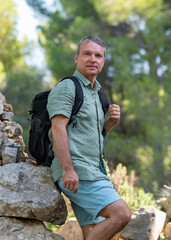Close-up portrait of a happy, smiling middle-aged man. A man is standing with a backpack, standing near small mountains. Concept - active lifestyle, travel, vacation