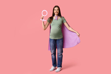 Beautiful young pregnant woman in superhero cape with gender symbol on pink background