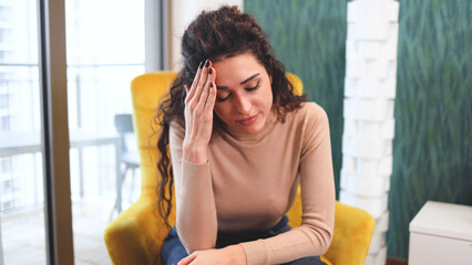 Beautiful mid adult woman having a headache, sitting at home and touching her forehead
