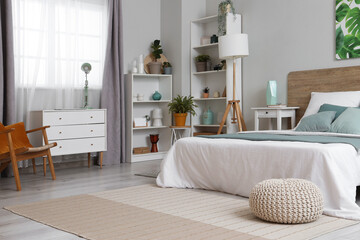 Beautiful interior of bedroom with soft bed, lamps, shelving units and bedside tables