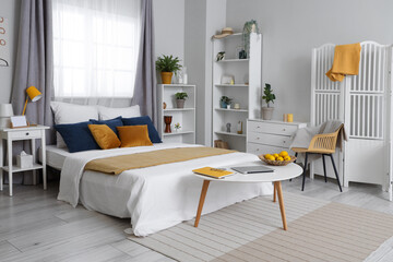 Modern interior of bedroom with comfortable bed, chest of drawers, shelving units and bedside tables