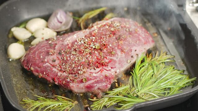 Ribeye steak with herbs and garlic are being roasted on the grill pan. 