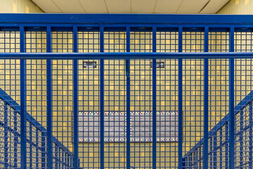 Close-up photo of a blue metal railing at the top of a school staircase and tile wall.