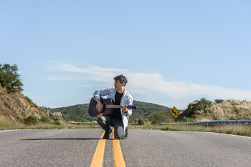 Músico y cantante con su guitarra arrodillado en medio de la carretera. Sensación de libertad, felicidad y bohemia.