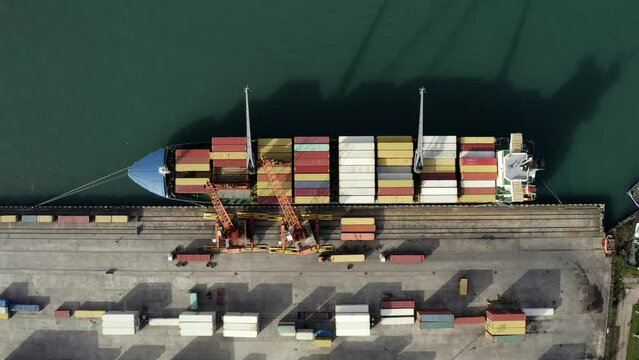 Top down aerial view of cargo ship loading containers. Showcases maritime shipping efficiency. Part of global distribution network.