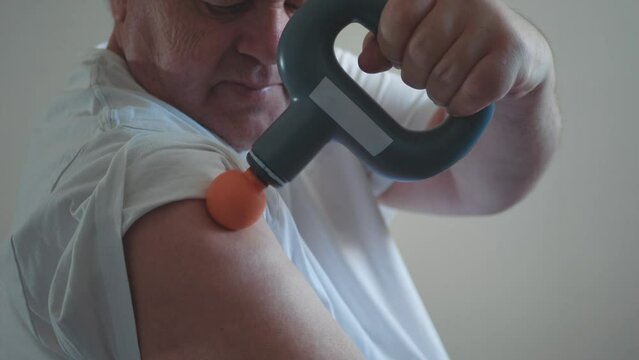 Massage percussion gun at work. Senior man massages arm muscles, care for failure in elderly with new technology.