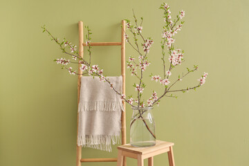 Vase with blooming branches on stepladder near green wall