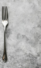 Single silver fork on a textured grey background with minimalist style.