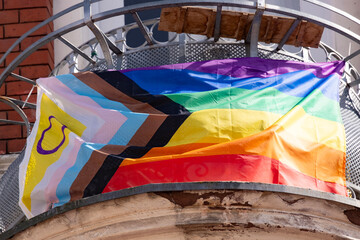 rainbow pride flag progress on balcony house, with black, brown, and blue lines trans flag in...