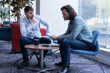 deux collègues discutent autour d'une table basse en buvant un café. Ils se détendent en travaillant - 781598021