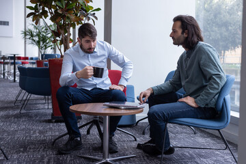 deux collègues discutent autour d'une table basse en buvant un café. Ils se détendent en travaillant - 781598030