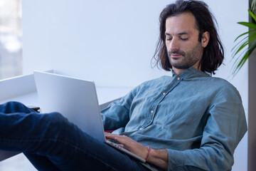 portrait d'un homme qui travaille dans un espace ouvert de co working. il est détendu et travaille avec un ordinateur portable sur ses genoux - 781598217