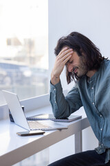 homme stressé et fatigué qui travaille devant un ordinateur portable. Il se tient la tête pour apaiser sa migraine et calmer son stress