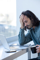 homme stressé et fatigué qui travaille devant un ordinateur portable. Il se tient la tête pour...
