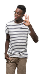 Young african american man wearing glasses and navy t-shirt smiling positive doing ok sign with hand and fingers. Successful expression.