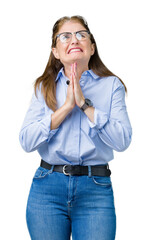 Beautiful middle age mature business woman wearing glasses over isolated background begging and praying with hands together with hope expression on face very emotional and worried.