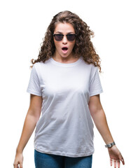 Beautiful brunette curly hair young girl wearing sunglasses over isolated background afraid and...