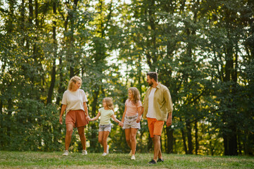 A joyful family is holding hands and taking a walk on meadow in nature