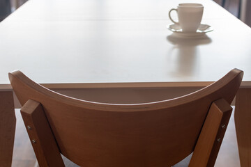 Furniture. Kitchen wooden chair closeup on blurred background of kitchen table with white cup