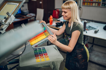 Fototapeta na wymiar Happy graphic worker is screen printing on manual printing press.