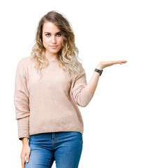 Beautiful young blonde woman wearing sweatershirt over isolated background smiling cheerful presenting and pointing with palm of hand looking at the camera.